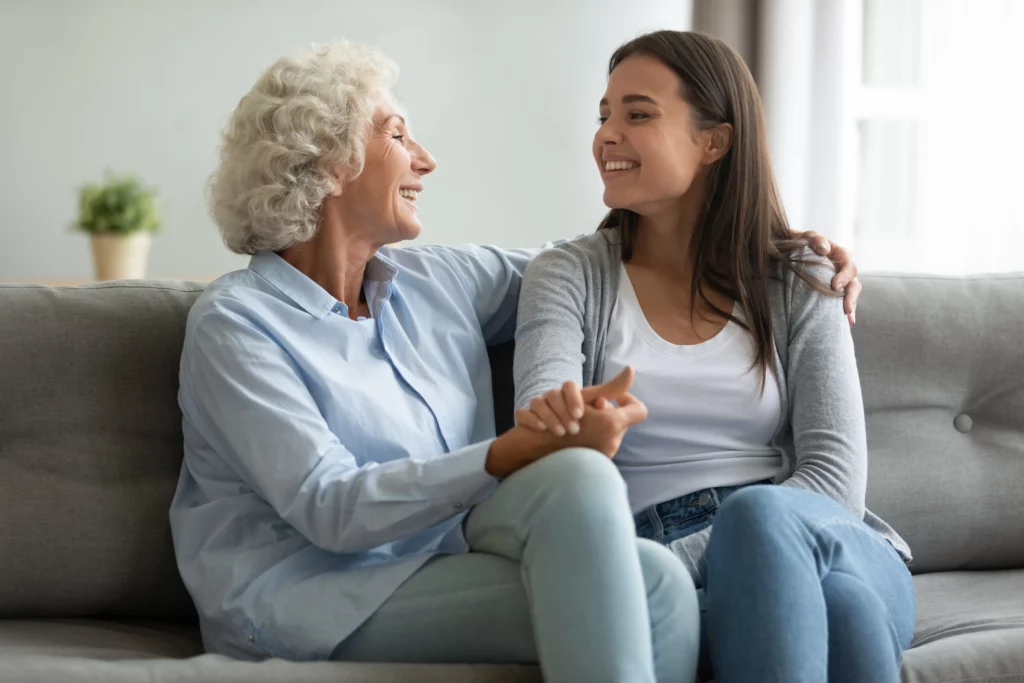 Smiling young woman holding hands with her grandmother on the couch, asking for financial support