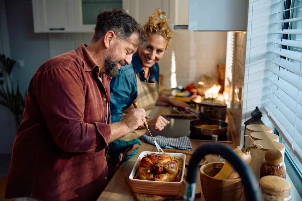 Happy husband and wife stand over the stove, probing a cooked roast chicken to test it