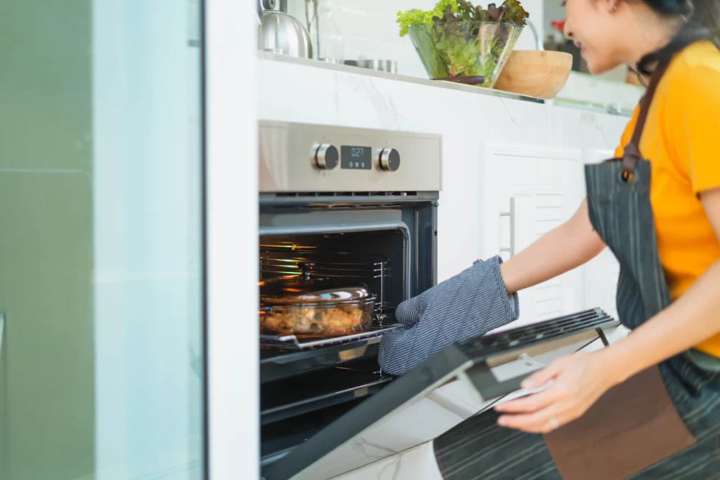 A woman wearing an apron pulls a roast dinner out of the oven