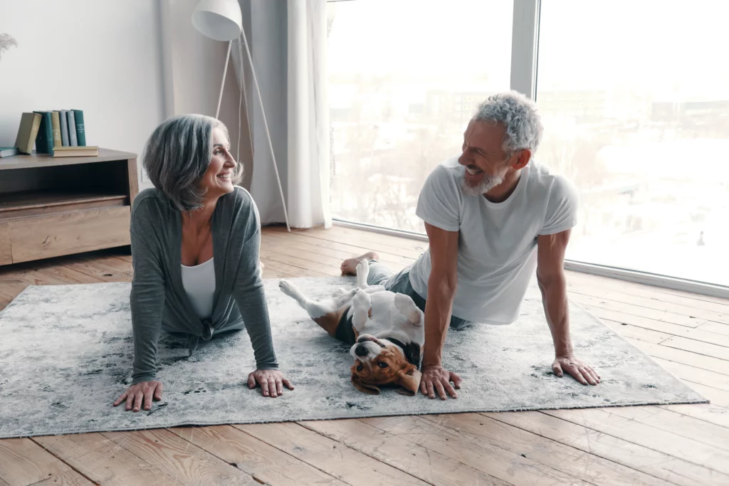 An older couple do yoga in their living room with their dog lying between them