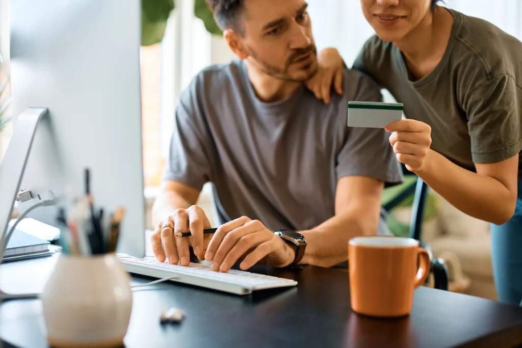 A couple sitting at a computer holding a credit card work on keeping their credit in good shape