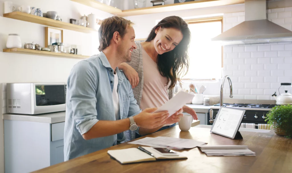 A happy couple sit at their kitchen island and go over their finances with bills and a tablet in front of them