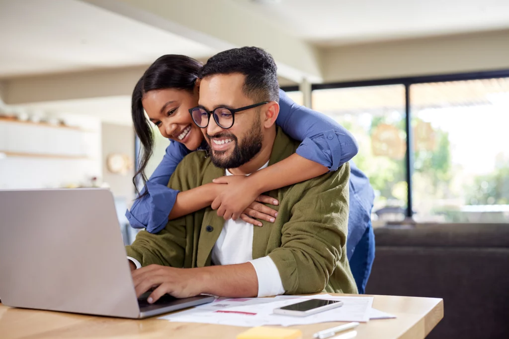 A smiling couple look over their finances on a laptop