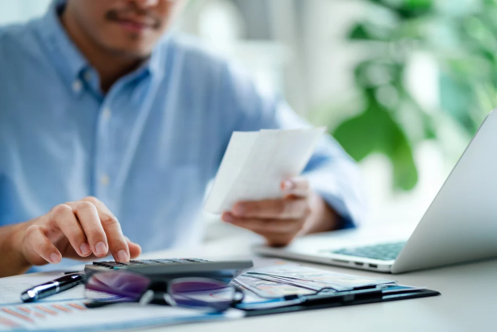 Close up of a man holding up receipts and adding them up with a calculator