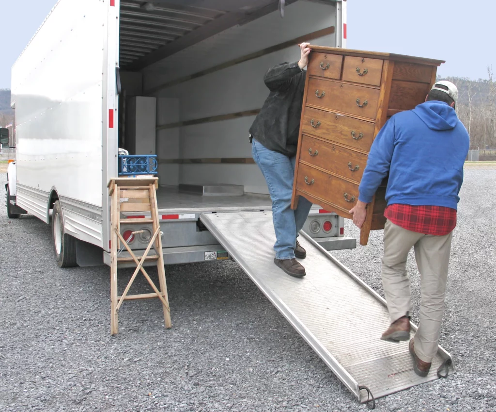 Two men carrying a heavy chest of drawers into a moving truck together