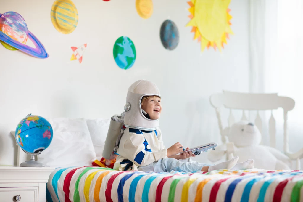 A child on a colourful bed dressed as an astronaut with planet stickers on the wall behind him