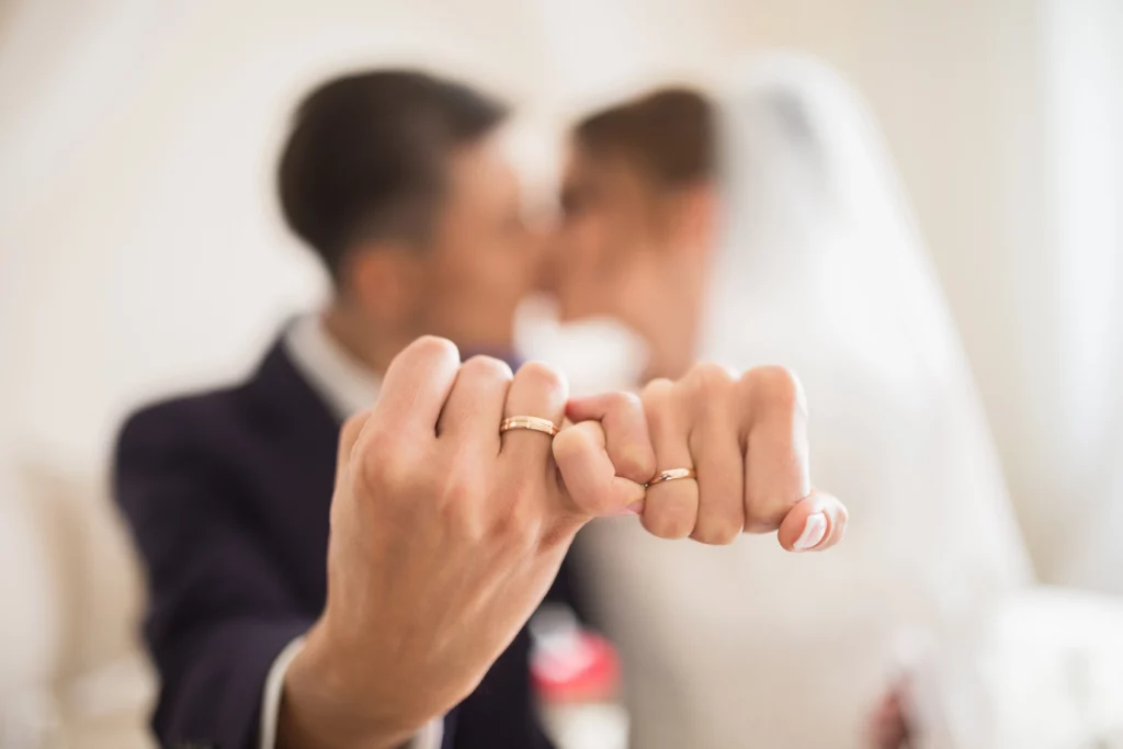 An out of focus bride and groom holding their hands out, pinkies wrapped around each other displaying their wedding rings
