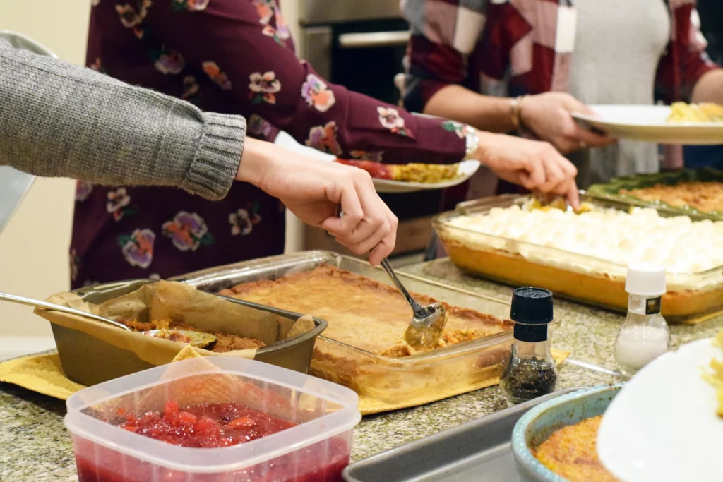 A close up of people grabbing food from a potluck