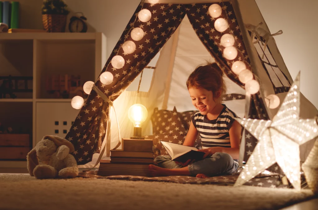 A young child reading in a warmly lit play area with plenty of lamps and floating bulbs