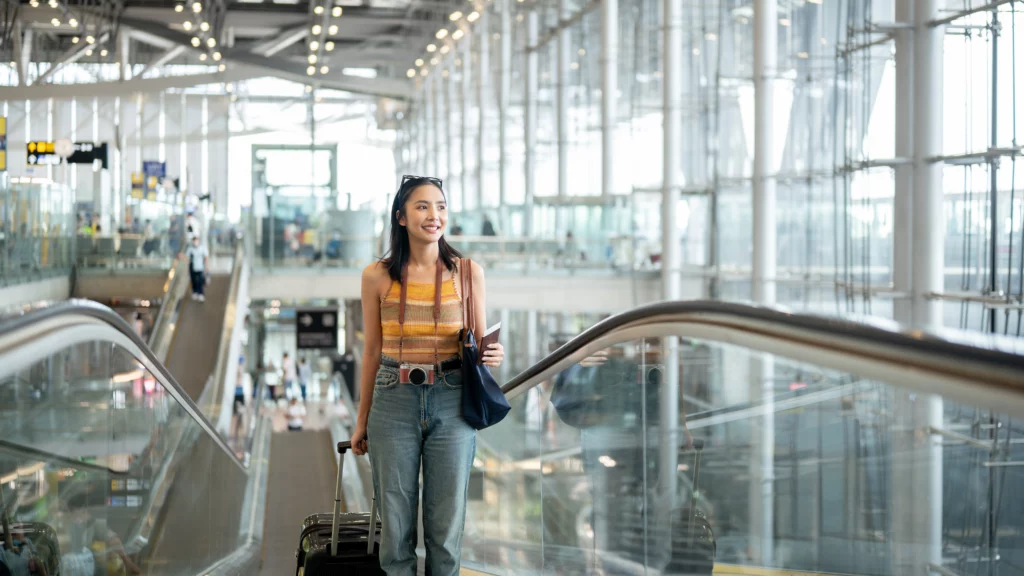 A woman with a suitcase comes up an escalator in an airport