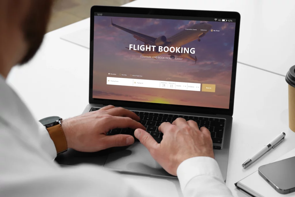 Close-up of a man's hands using a laptop with a flight booking website on the screen